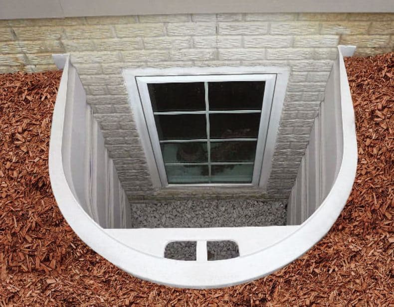 Window well filled with gravel and surrounded by wood mulch, showing an exterior view.