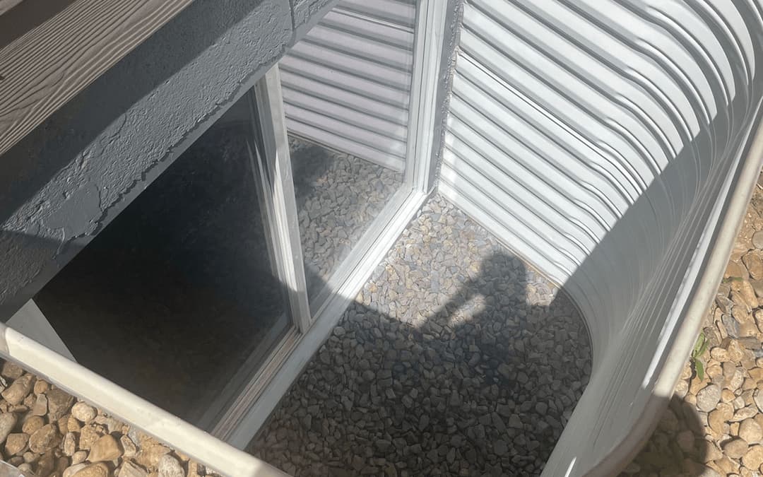Window well with gravel base and sunlight casting a shadow, enhancing drainage function.