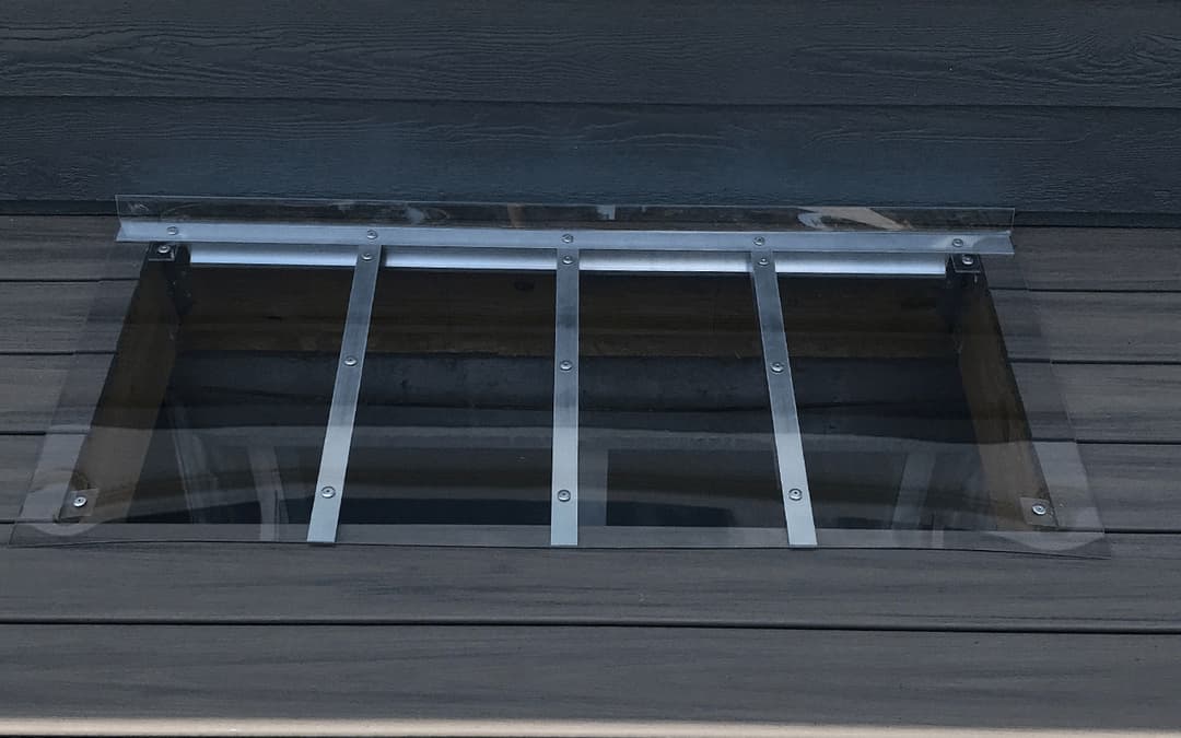 Transparent skylight with metal bars on wooden deck surface, enhancing natural light indoors.