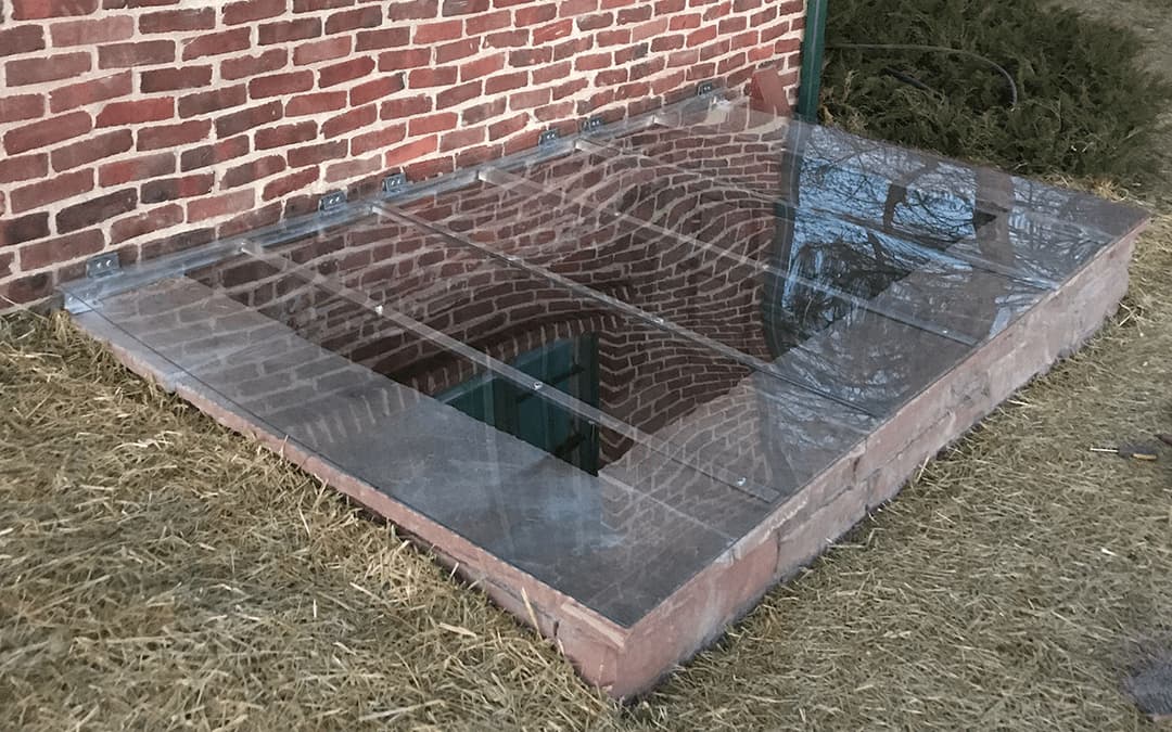 Glass-covered basement entrance with brick walls and grass around the opening.
