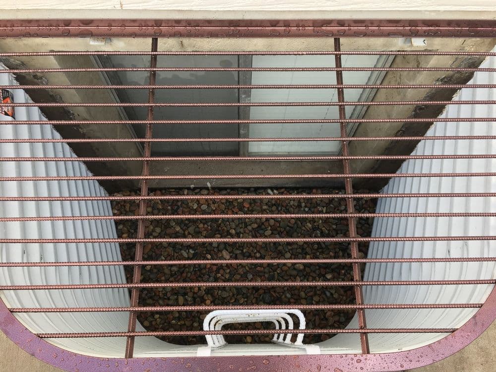 View of a gated window well filled with rocks, from a top-down perspective.